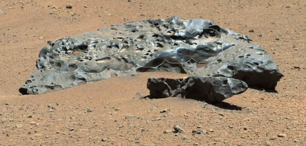 A black, rocky meteorite on a sandy surface