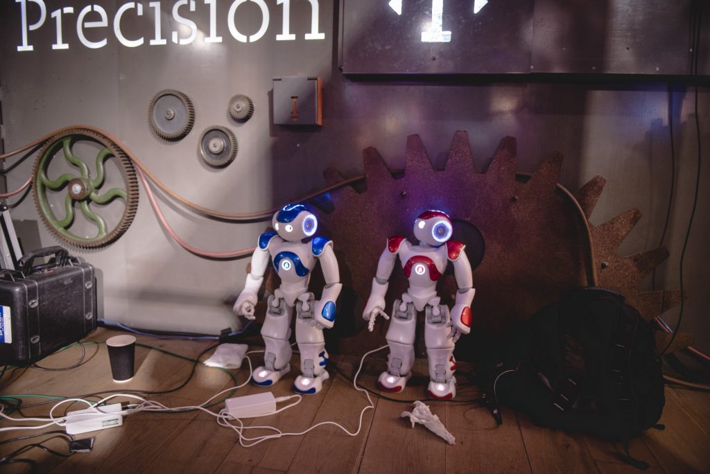 Two small humanoid robots stand as if they are waiting to do something. 