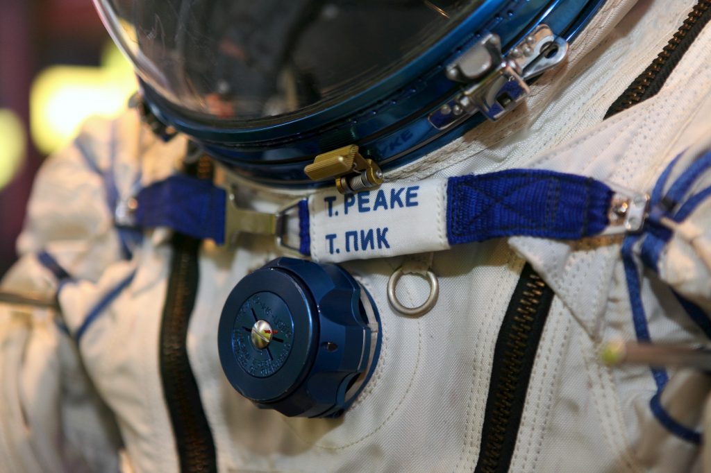 A detail of Tim Peake's spacesuit - a closeup showing the name badge reading "T. Peake" just below the helmet visor, and a blue valve on the front of the suit
