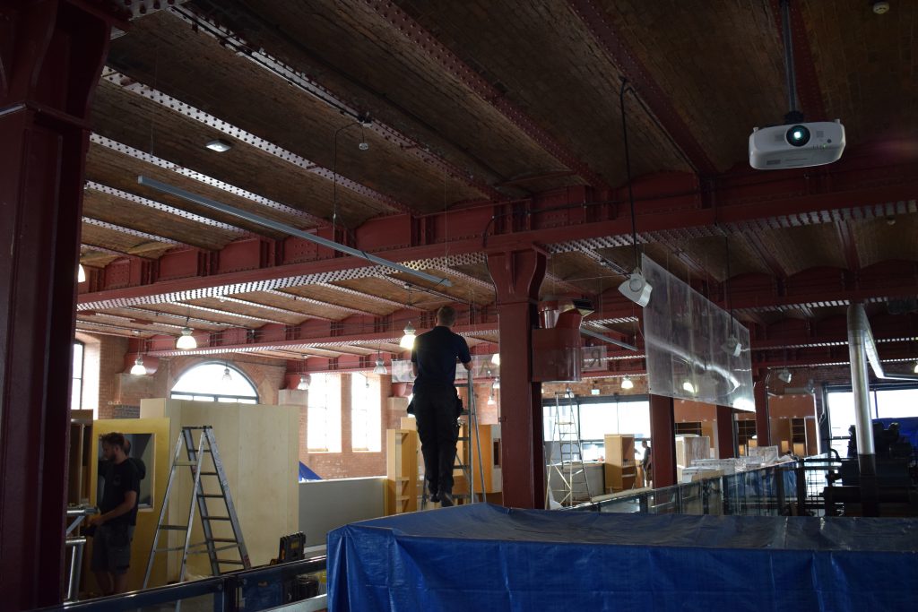 A man climbs up a ladder during the textiles gallery refresh