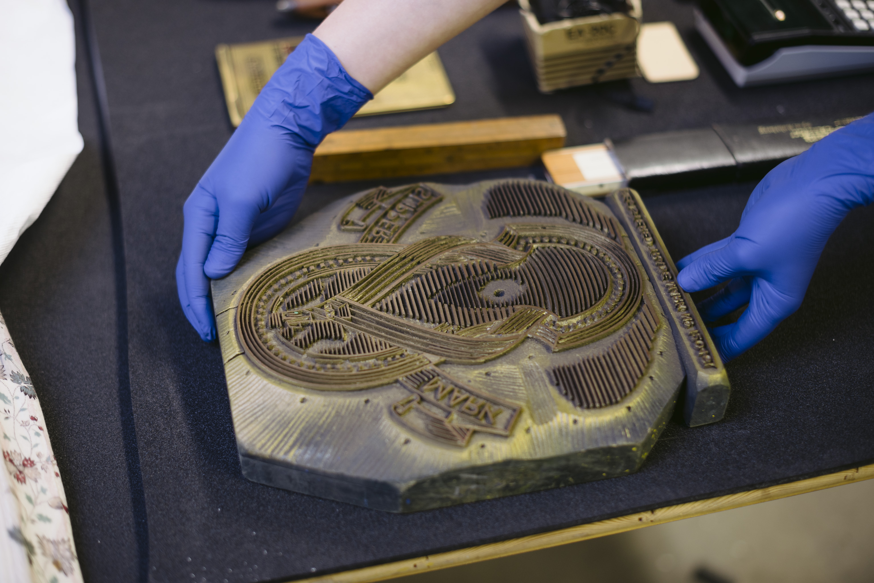 An onate stamping block with a looping pattern is being lifted by a woman wearing a pair of blue gloves
