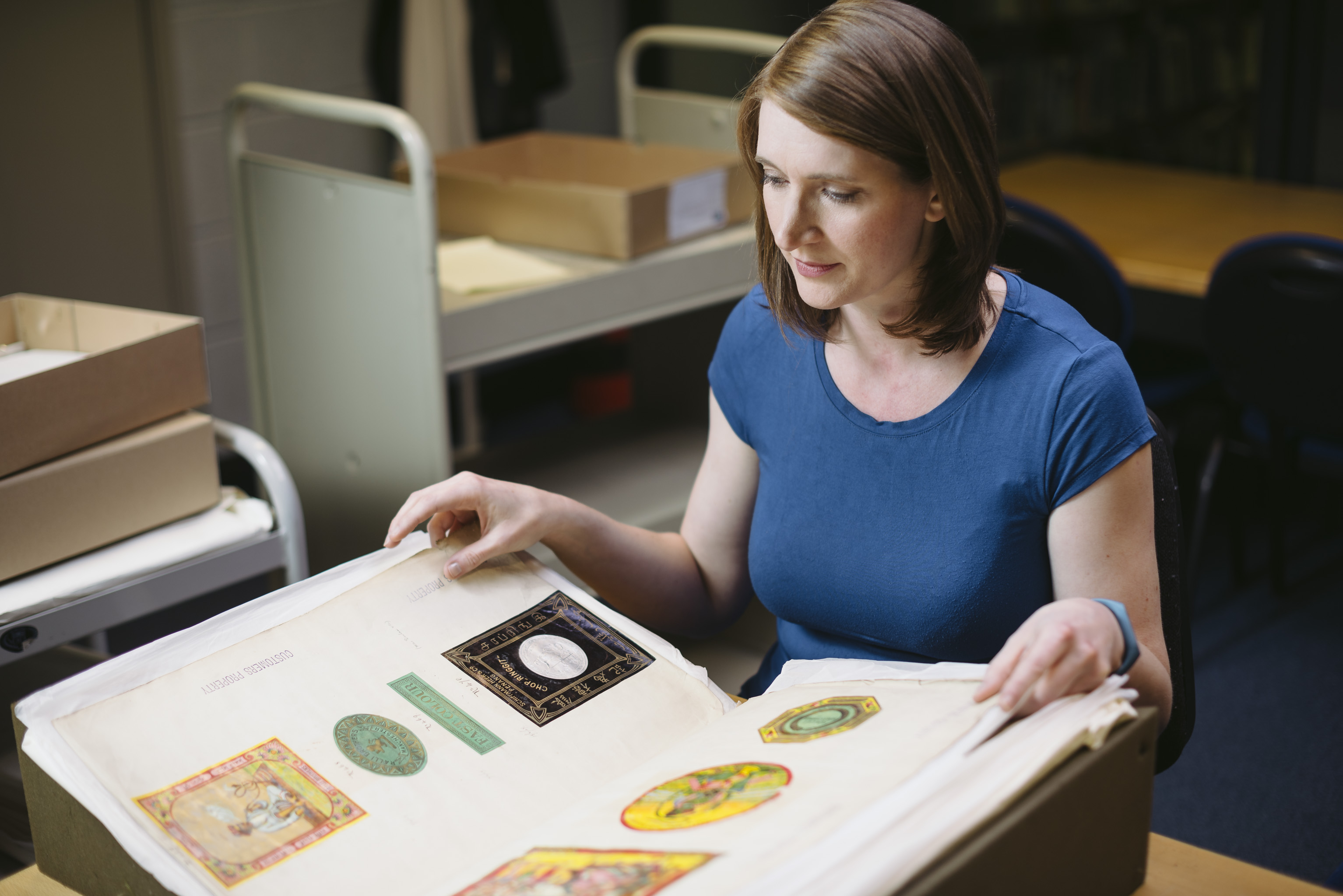 A woman in a blue top leafs through a large album containing colourful images. 