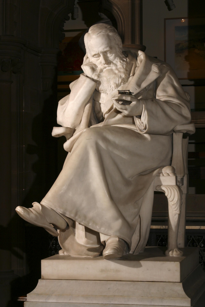 A marble statue of an old man sitting with his head resting on one hand - a representation of the scientist James Joule