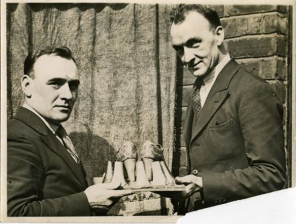 Sepia photo of two men holding high heel shoe samples