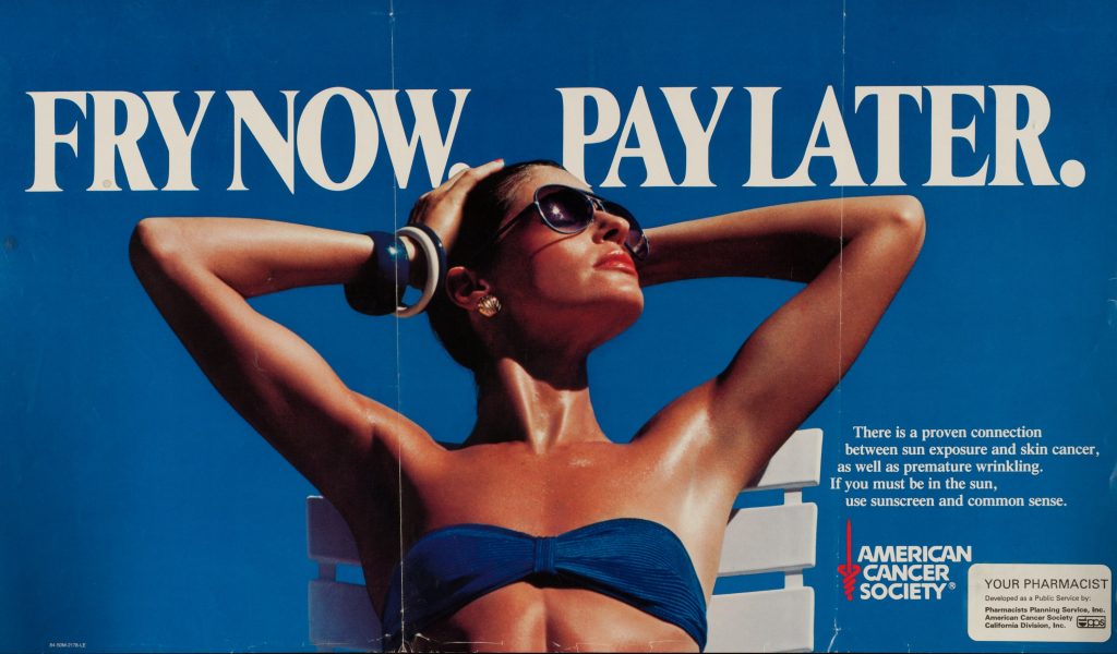 A poster showing a woman sunbathing against a blue background, with the text "Fry Now Pay Later", on display in the exhibition The Sun, at the Science and Industry Museum in Manchester