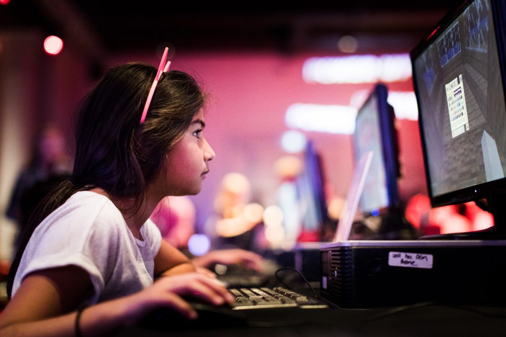 A girl wearing pink cat ears looks intently at a computer screen where she is playing a game
