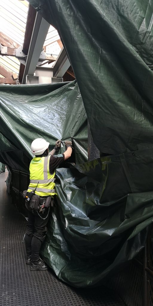 A man in a white hard hat and yellow hi-viz reaches to fix two tarpaulins together in the Science and Industry Museum's Power Hall