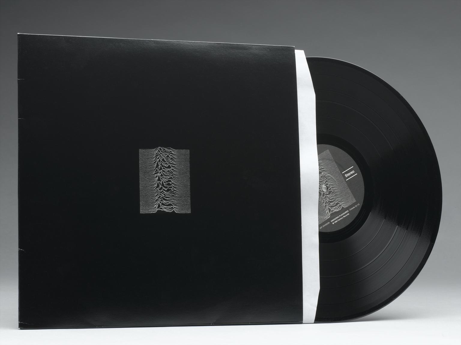 A vinyl record of the album Unknown Pleasures by Joy Division. It is half out of the sleeve. The sleeve is black with a small design of white wavy lines at the centre.