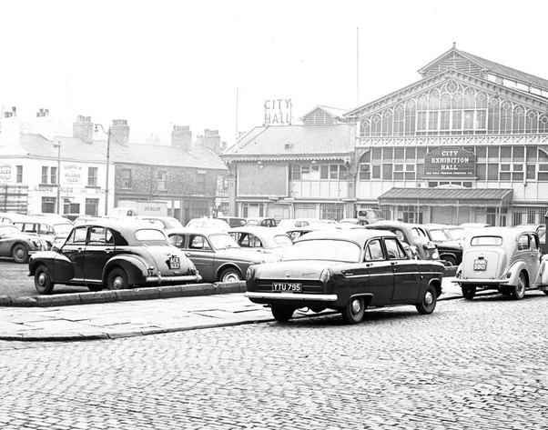 Black and white photo of old cars parked outside a market hall
