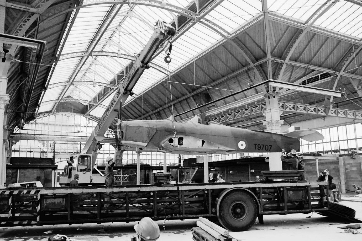 Black and white photo of a plane being hung from the ceiling of an old market hall