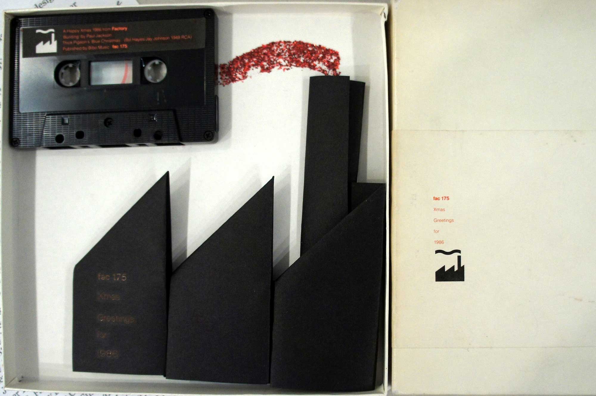 A white box with a black cassette tape and a model of a factory made out of black card in it