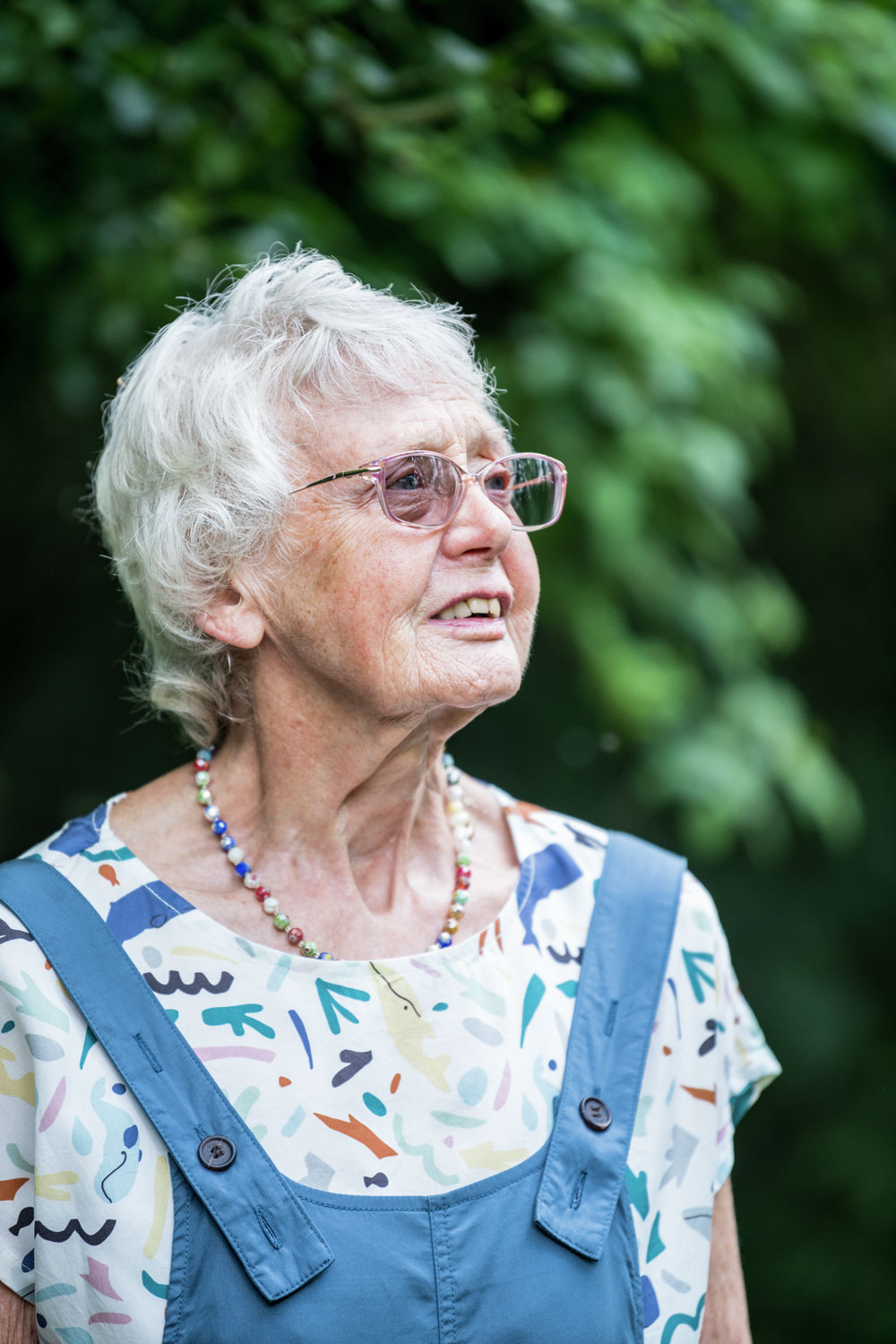 An older woman with grey hair, glasses and dungarees, looking off to the side