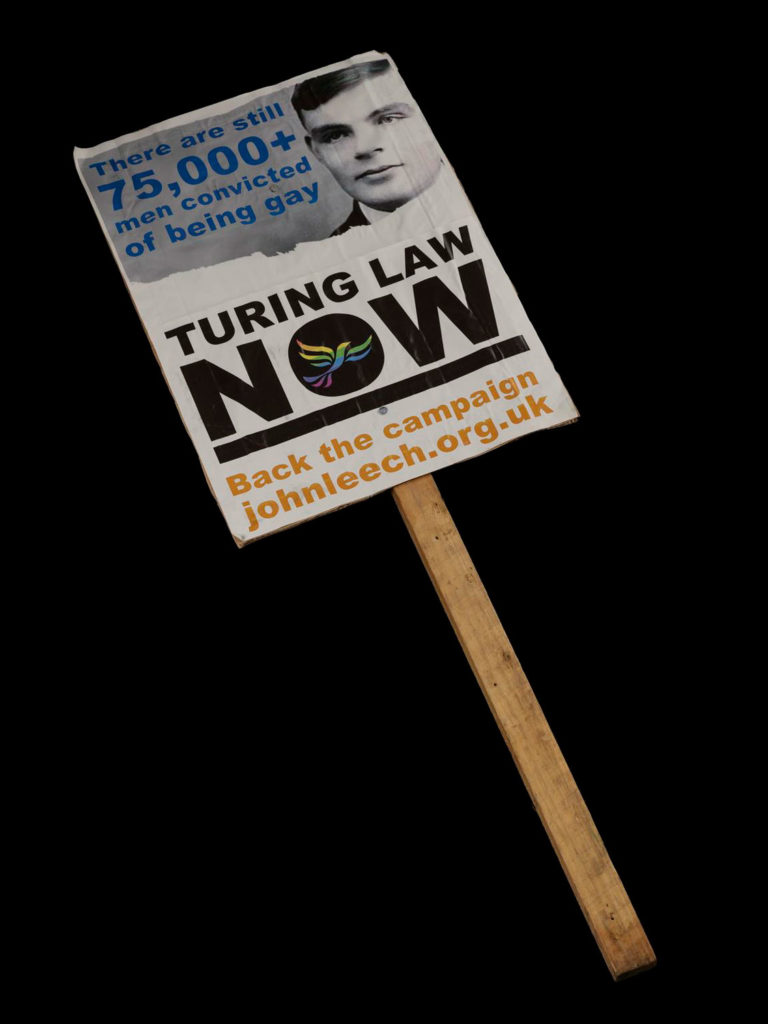 A placard with a picture of Alan Turing and a demand for his pardon written on it.