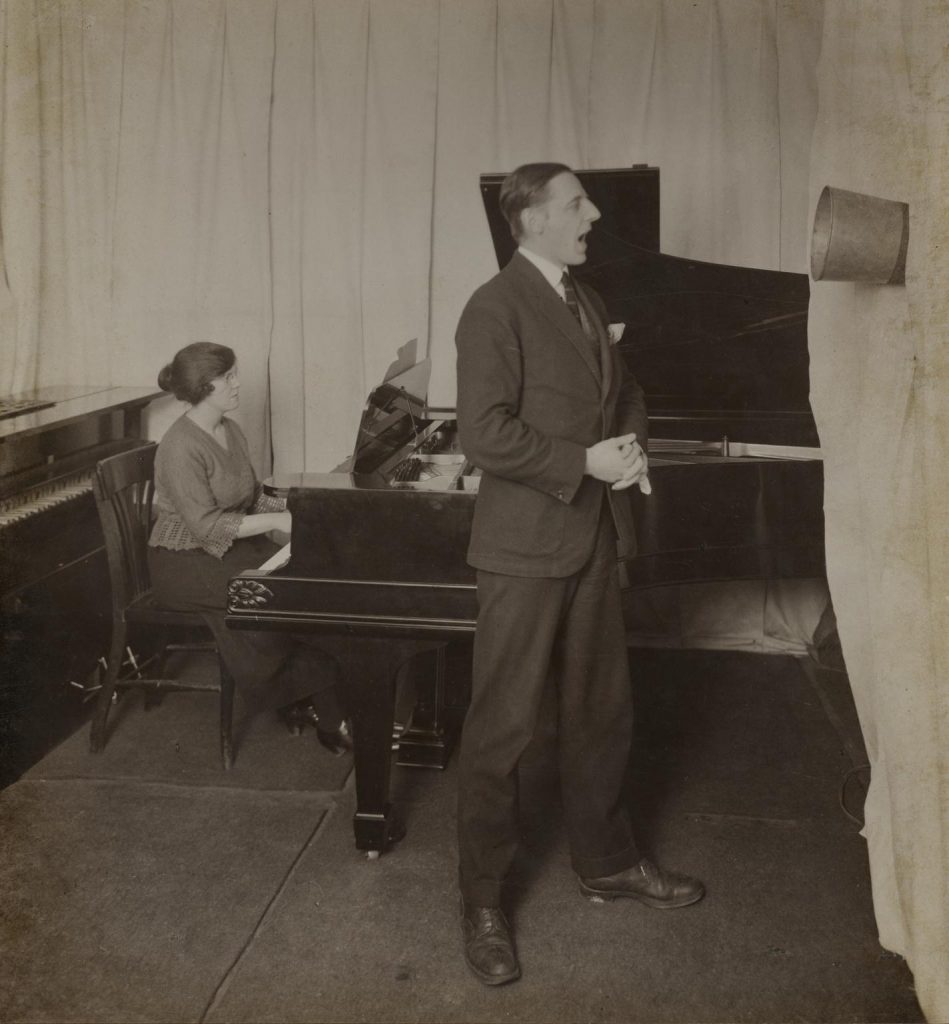 Sepia photo of a man singing and a woman playing piano.