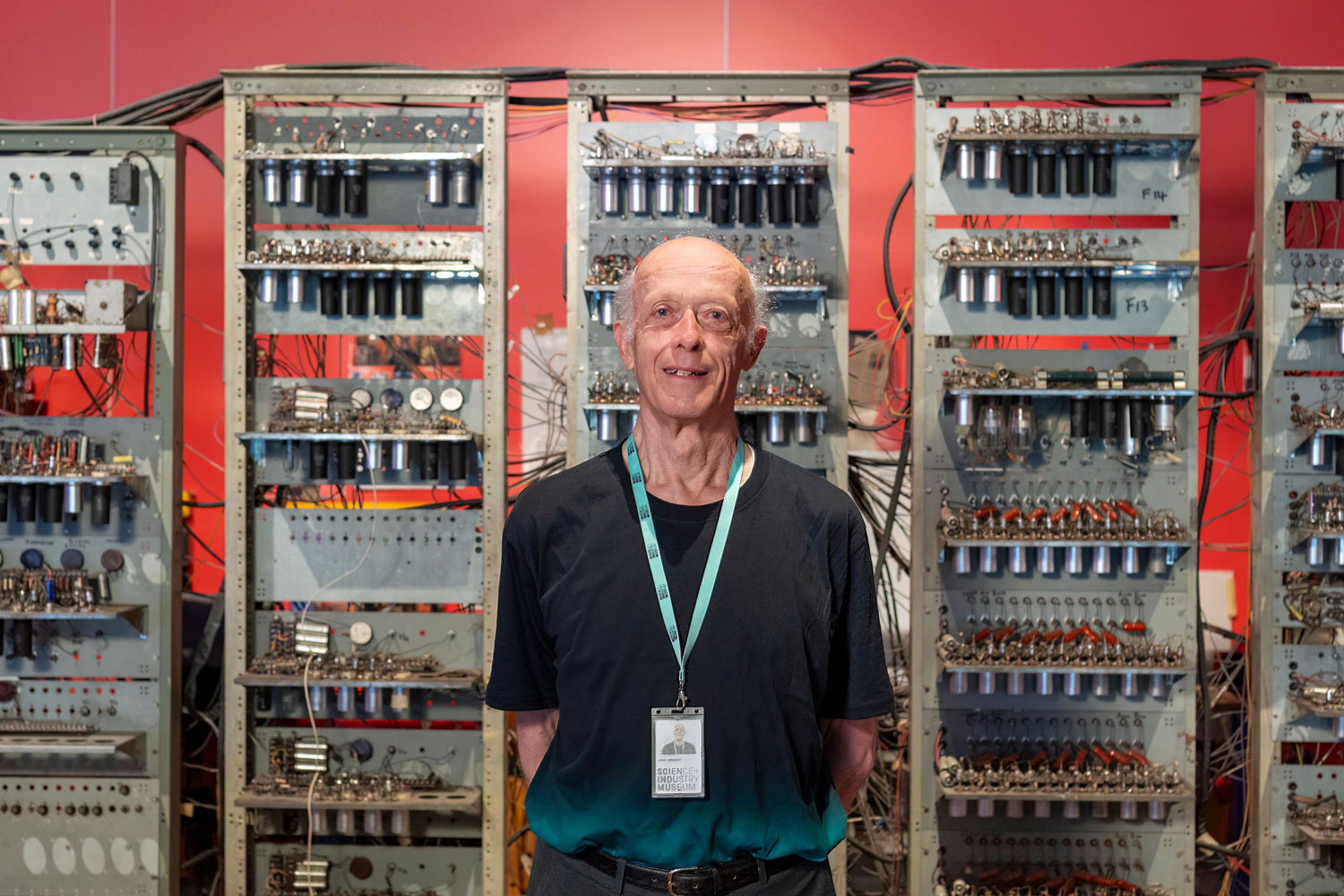 An older man in a museum uniform stood in front of an early computer.