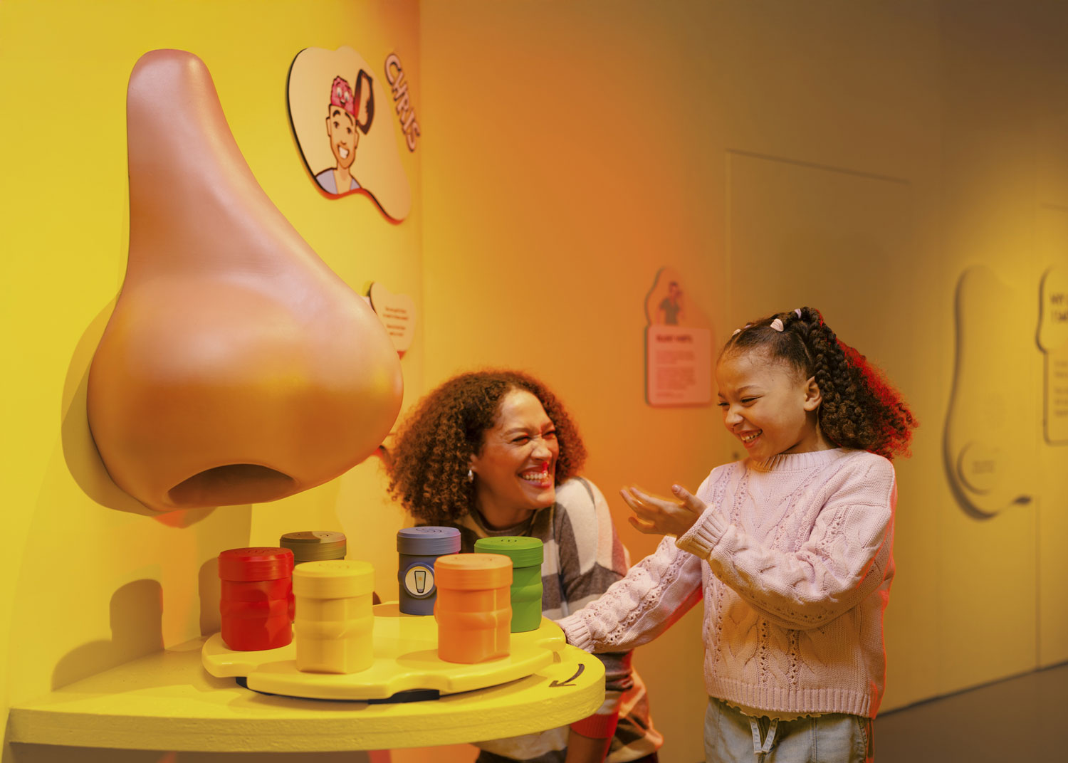 A mother and daughter playing with an interactive museum display shaped like a giant nose