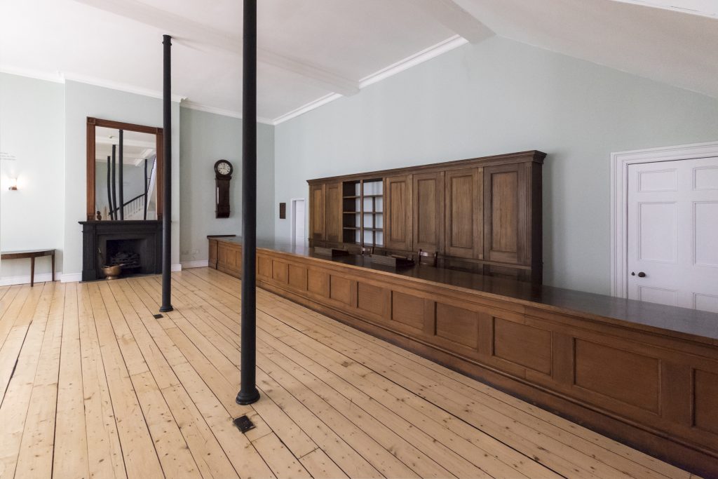 An old fashioned railway station booking hall with wooden floors, wooden counters and pale walls