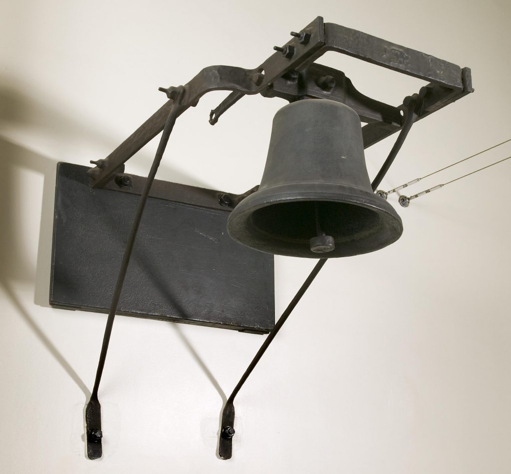 A large black bell photographed against a white wall