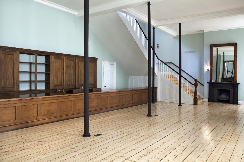 The first class booking office at Liverpool Road Station - a room with pale floors and pale green walls, with a long wooden counter running along one side