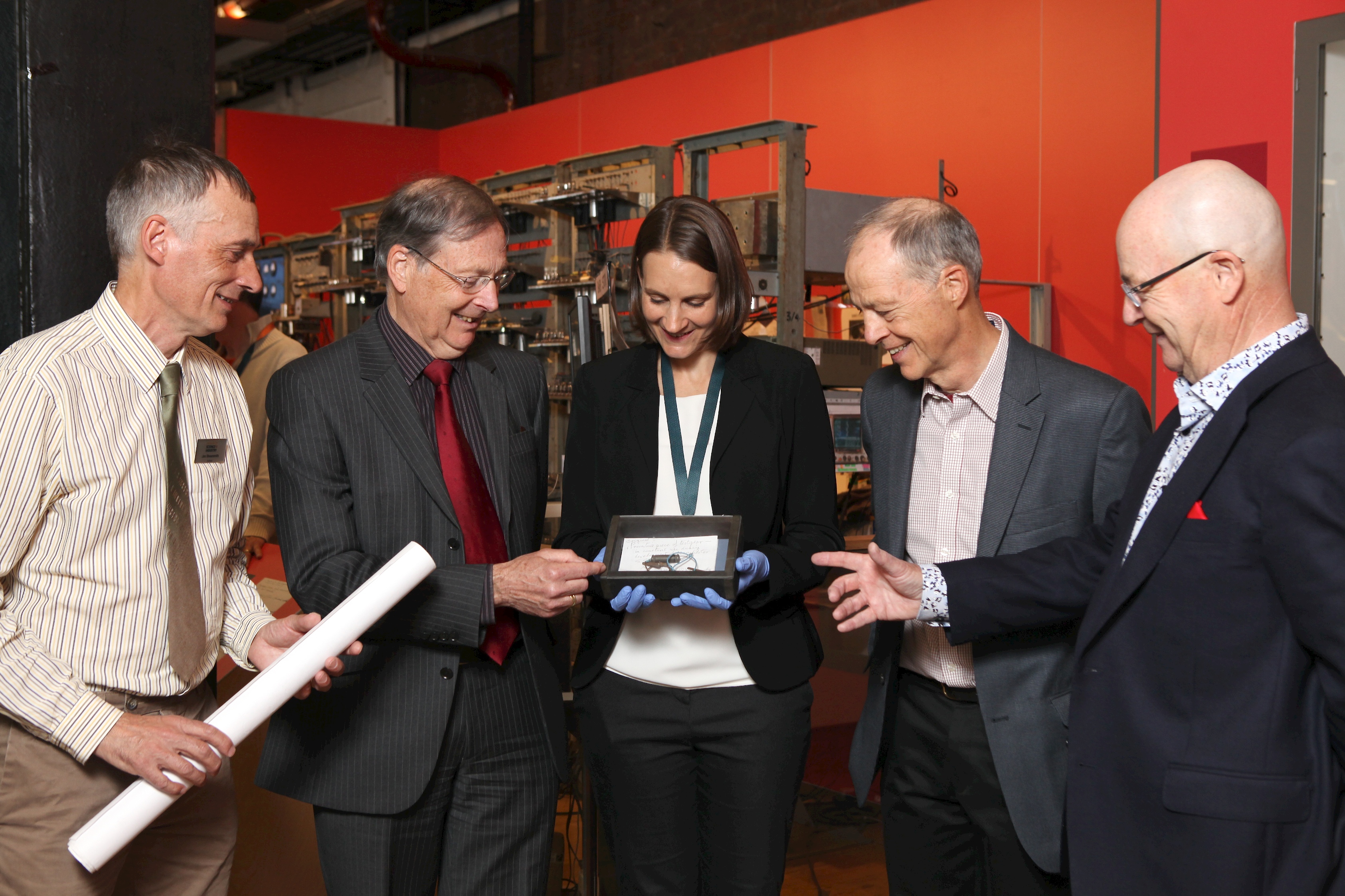 Four men and a woman looking at an object inside a black box 