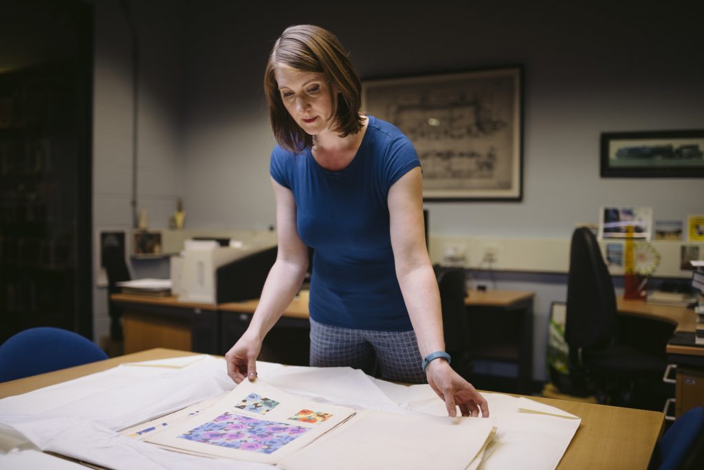 A woman in a blue top looks through sheets of floral designs