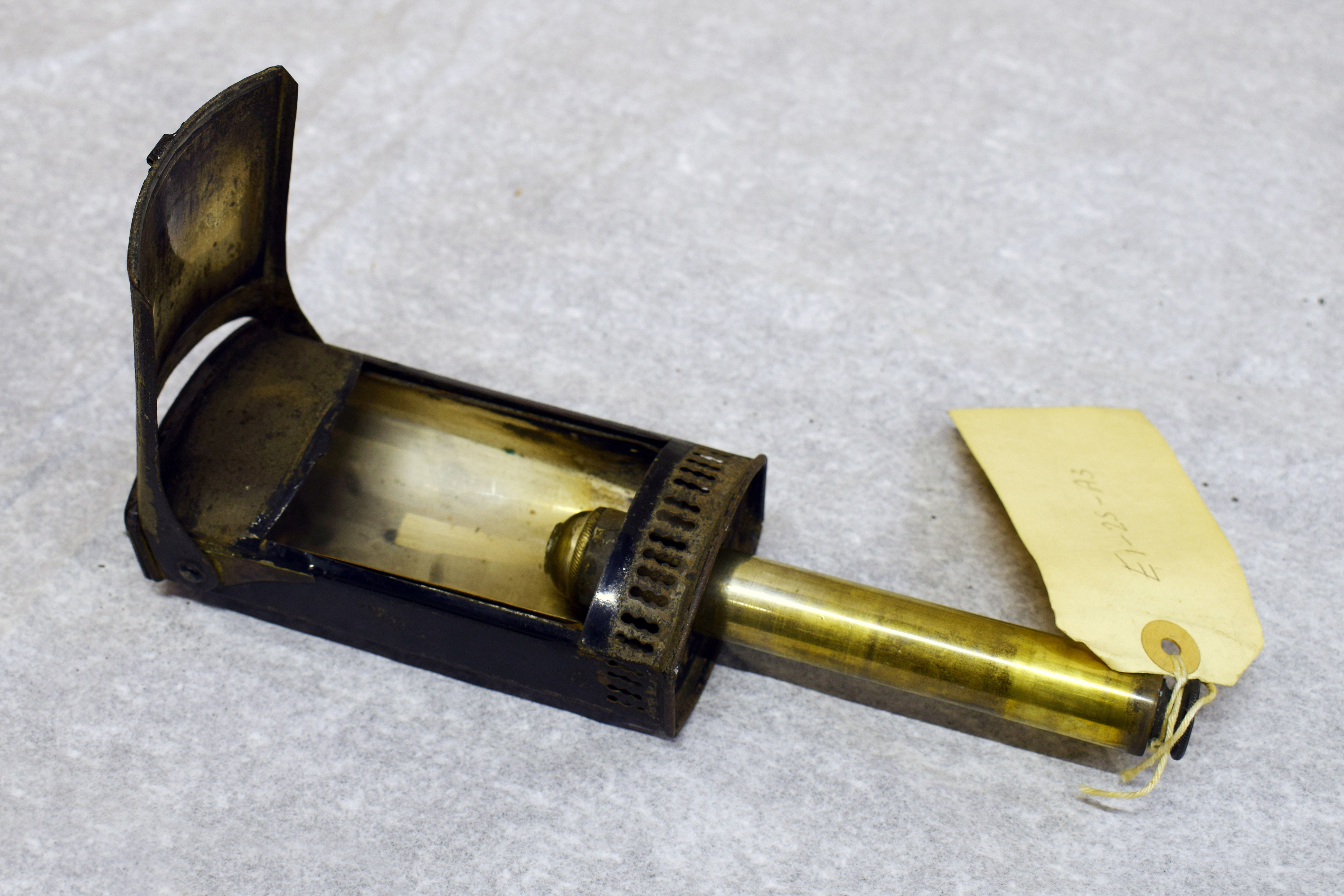 A black metal box with an open lid at the front, showing a rod has been extended from inside to come out at the bottom