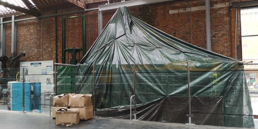 A huge machine is covered by green tarpaulin in the Science and Industry Museum's Power Hall