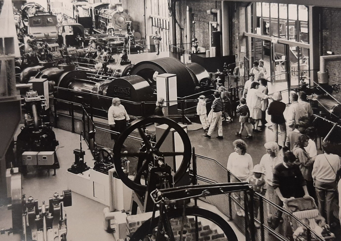 Black and white photo of visitors exploring a room full of machines