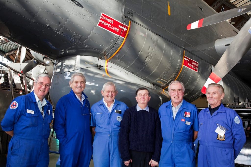 Six men in blue overalls stood in front of a plane