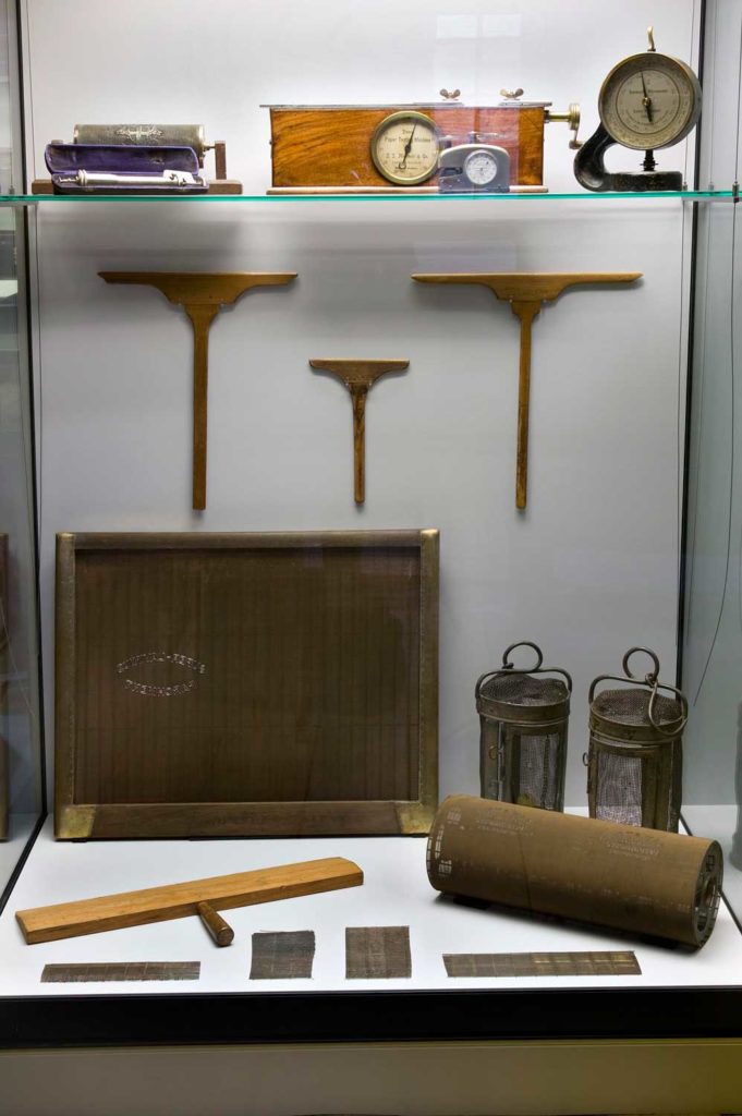 A glass cabinet containing old papermaking equipment