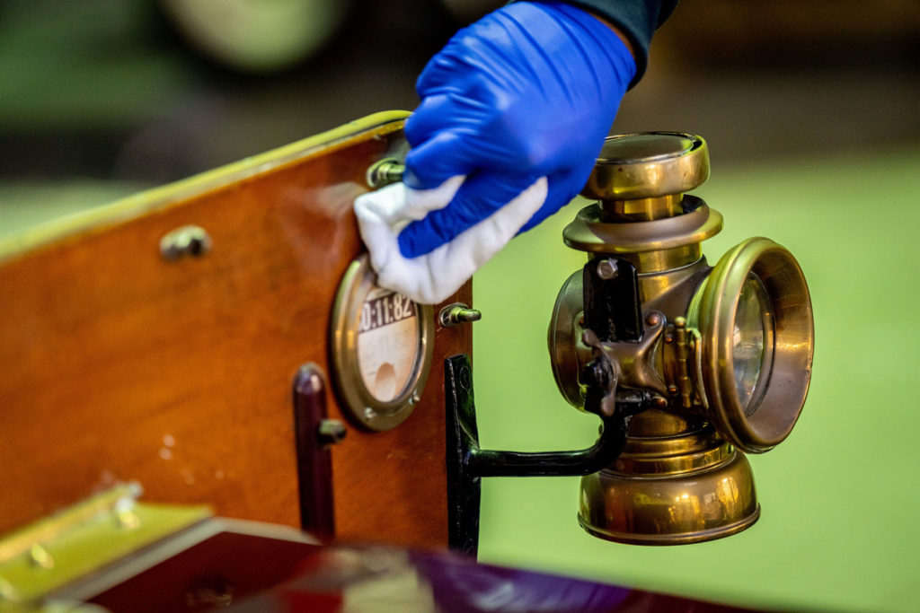 A hand in a blue glove cleaning the dashboard of an old car