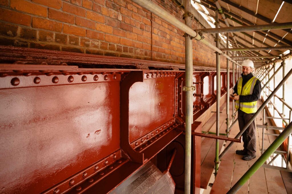 A man stood on a platform looking at a metal girder painted red