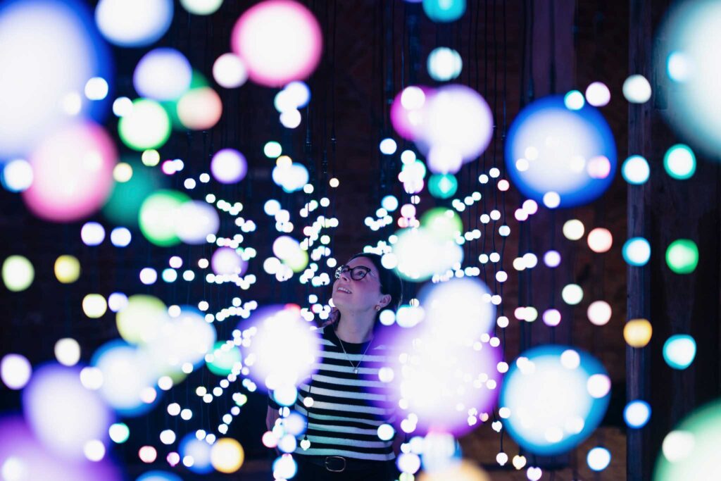 A woman in a striped top looking at white spherical lights hanging from the ceiling of a warehouse
