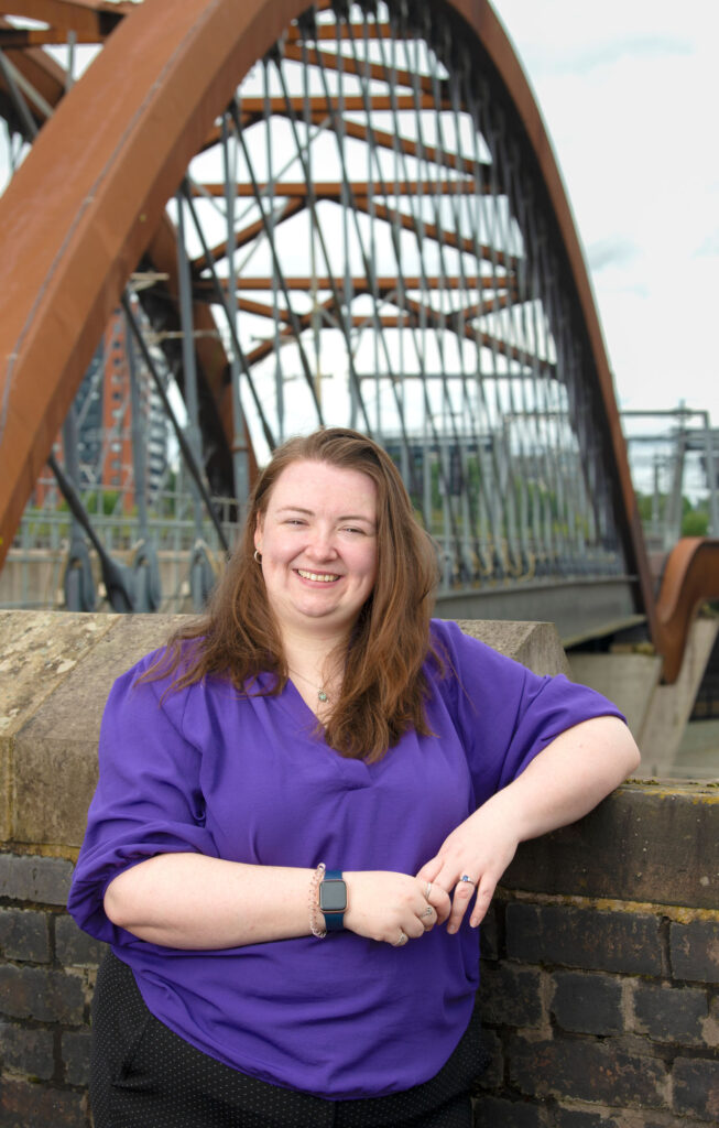 A woman posing for a photo in front of a railway bridge
