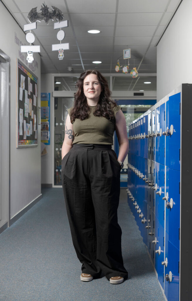A woman stood next to some lockers in a primary school corridor
