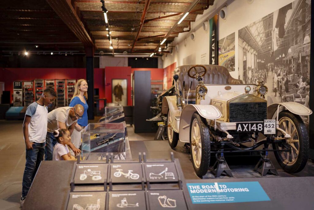 A man, a woman and and a small child looking at an early Rolls Royce car on display in a museum