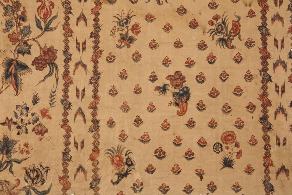 A chintz panel, printed with trailing vines of exotic flowers and fruit between bands of chevrons, the ground sprigged with small flowers.